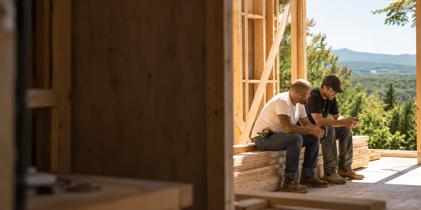 Two carpenters taking a break at a sunlit timber-frame job site